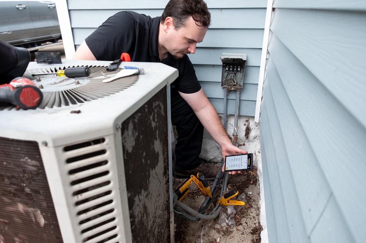 Technician servicing an outdoor HVAC air conditioning unit mounted on a residential home exterior